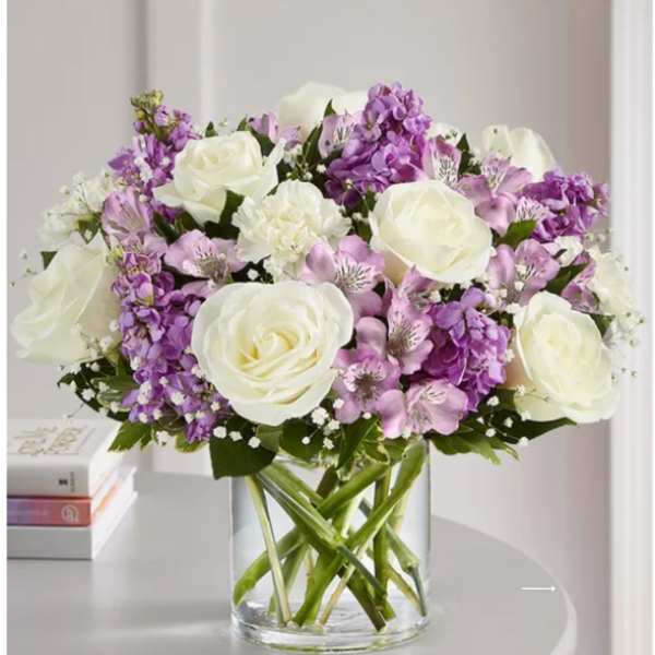 Bouquet of white roses and purple flowers in a clear glass vase