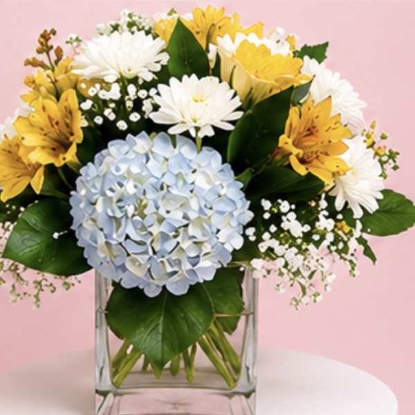 Bouquet of yellow and white flowers with a blue hydrangea in a clear glass vase