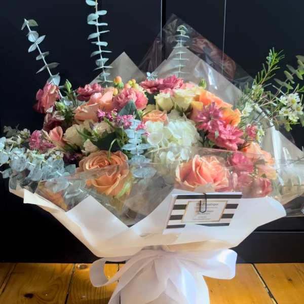 Bouquet of peach and pink roses with white hydrangea in clear wrap