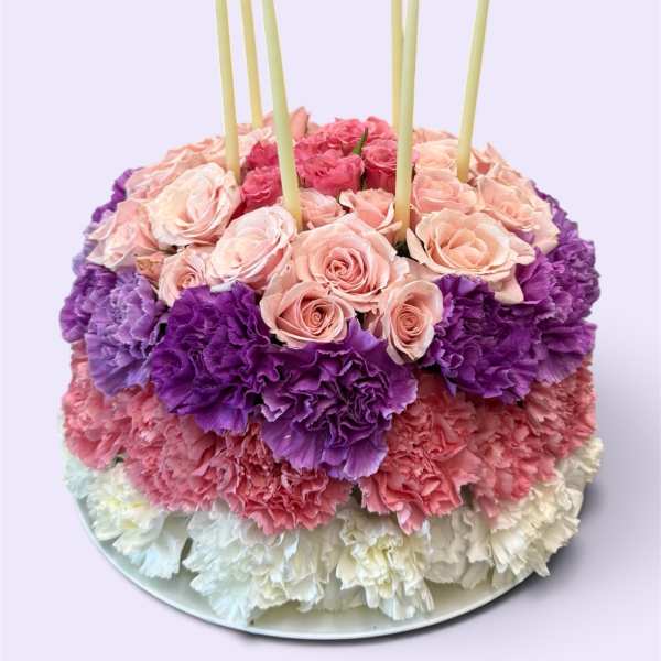 Round floral cake with pink roses, purple carnations, and white candles