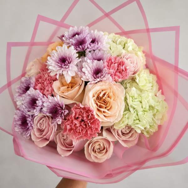 Bouquet of pink and peach roses with purple daisies and hydrangeas in pink wrap