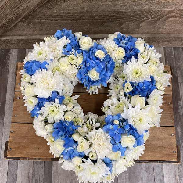 Heart-shaped floral wreath with white and blue flowers on a wooden surface