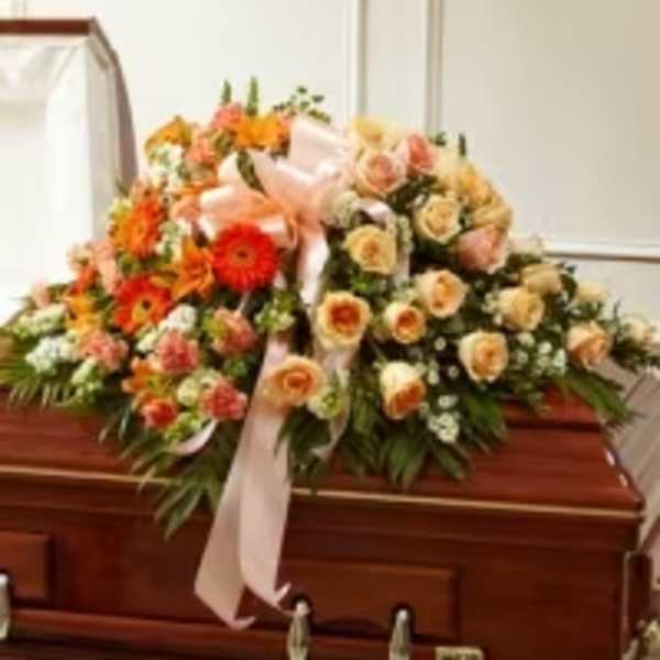 Large floral casket spray with peach, orange, and cream flowers and a pink ribbon