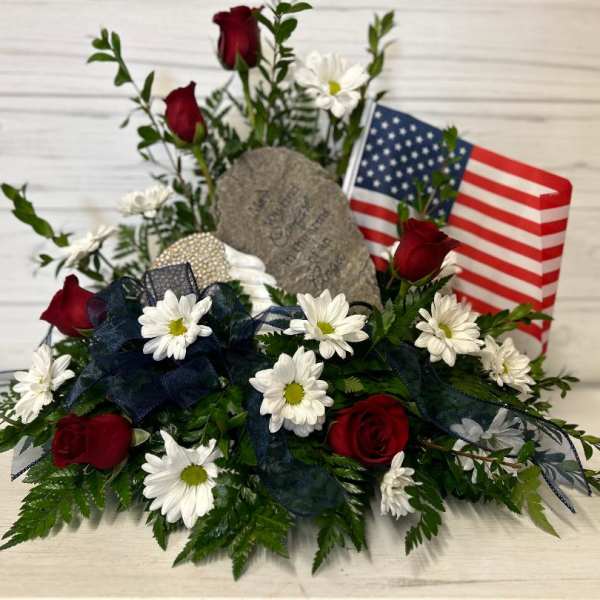 Red roses and white daisies arranged with an American flag and memorial stone.