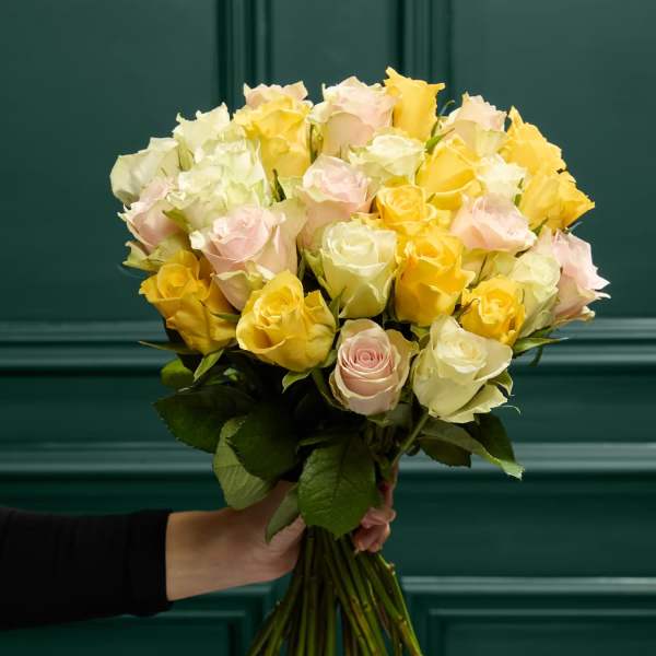 Handheld bouquet of pale yellow, cream, and blush roses