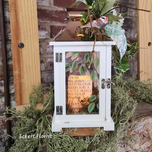 White lantern with greenery and a memorial message
