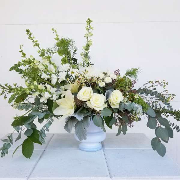 White floral arrangement in a white urn with long greenery