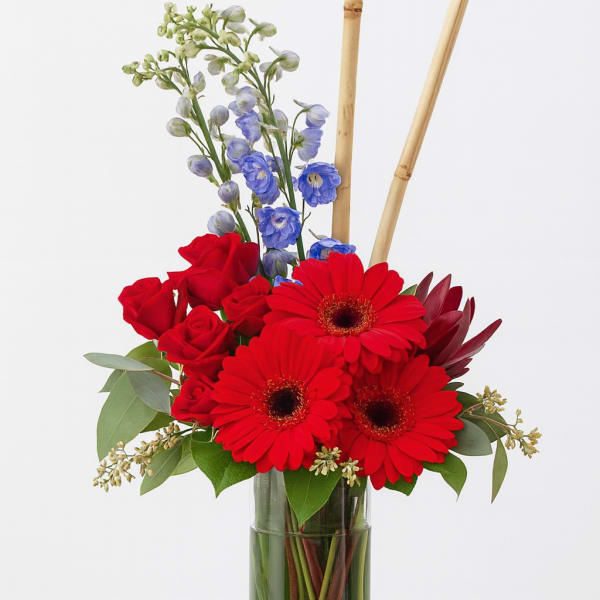 Red gerberas and roses in a glass vase with blue flowers