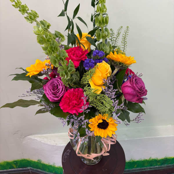 Mixed bouquet of roses, carnations, and sunflowers in a glass vase