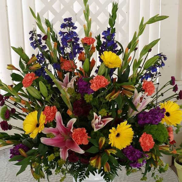 Large mixed flower arrangement in a white pedestal vase