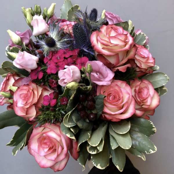 Bouquet of pink roses and lisianthus with dark thistle accents