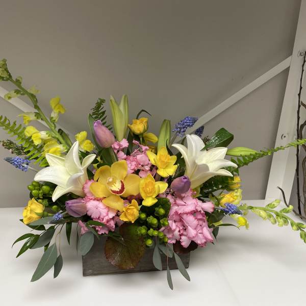 Mixed bouquet with white lilies, yellow orchids, and pink carnations in a wooden container