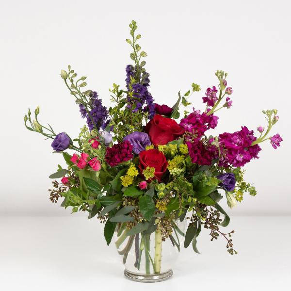 Mixed bouquet of red, pink, and purple flowers in a clear glass vase