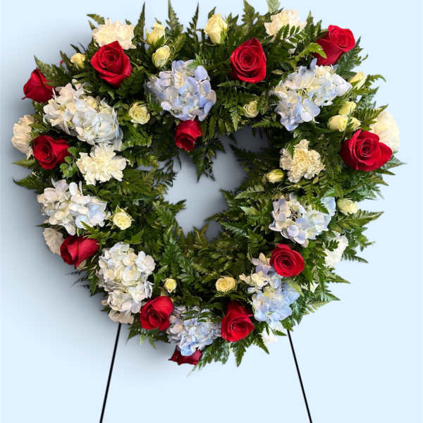 Heart-shaped floral wreath with red roses and pale hydrangeas on a stand