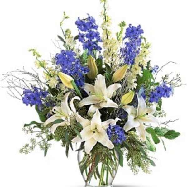 Tall arrangement of white lilies and blue flowers in a clear glass vase