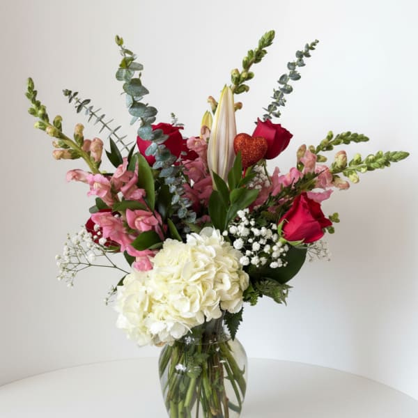 Mixed bouquet with red roses, white hydrangea, pink blooms, and a glass vase