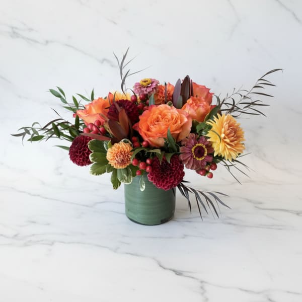 Orange and burgundy floral arrangement in a green vase