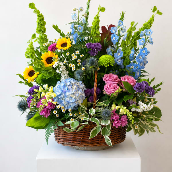 Mixed flower basket with sunflowers, blue hydrangea, pink roses, and purple blooms