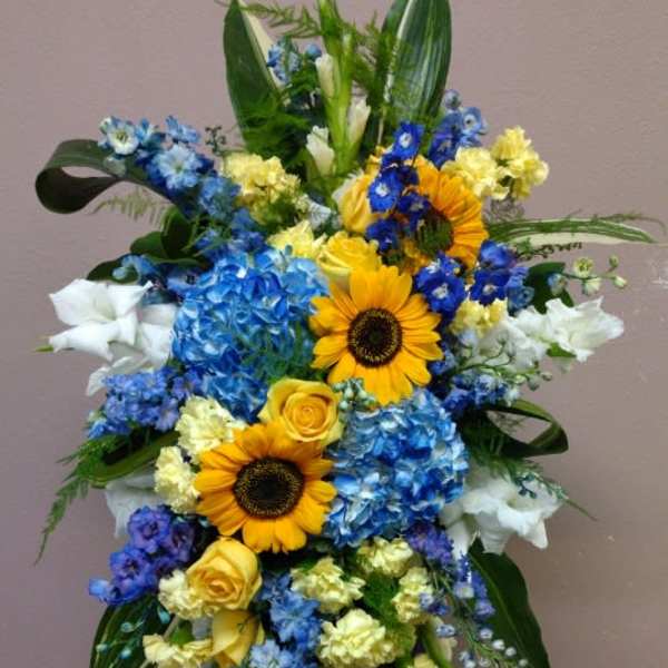Tall standing floral spray with sunflowers, blue hydrangeas, and white blooms