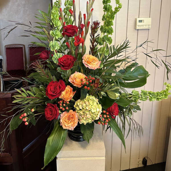 Tall arrangement of red and peach roses with green hydrangea and Bells of Ireland in a black vase