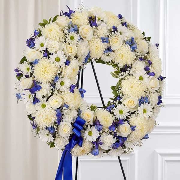 White floral wreath with blue accents on a black stand