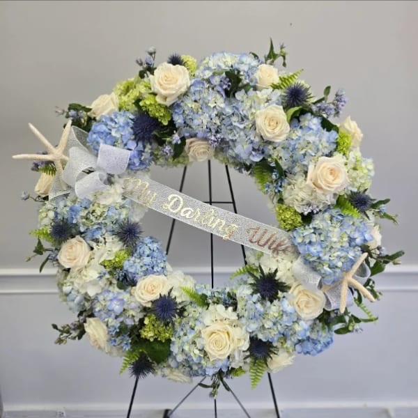 Circular floral wreath with blue hydrangeas, white roses, and starfish accents