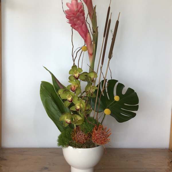 Tall tropical arrangement with pink blooms and green orchids in a white vase