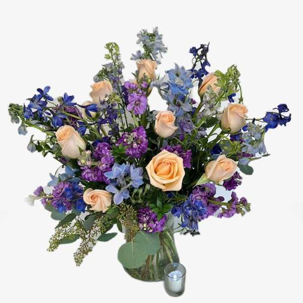 Peach roses and blue-purple flowers in a glass vase with a candle