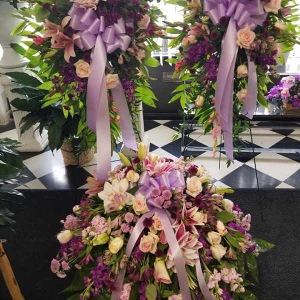 Three large floral standing sprays with lavender ribbons and mixed pink-purple blooms
