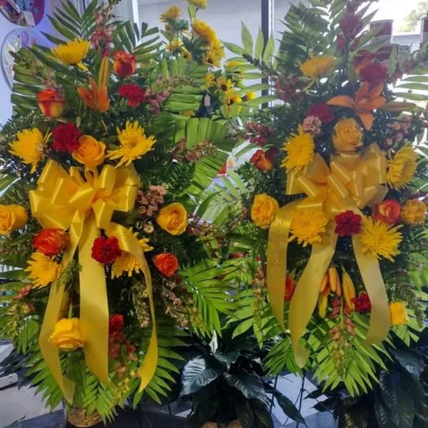 Two large floral standing sprays with yellow ribbons and mixed blooms