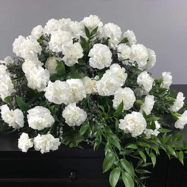 White carnation funeral spray on a dark casket