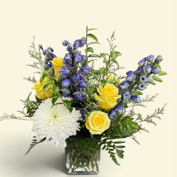 Yellow roses and white chrysanthemum in a glass vase with blue flowers