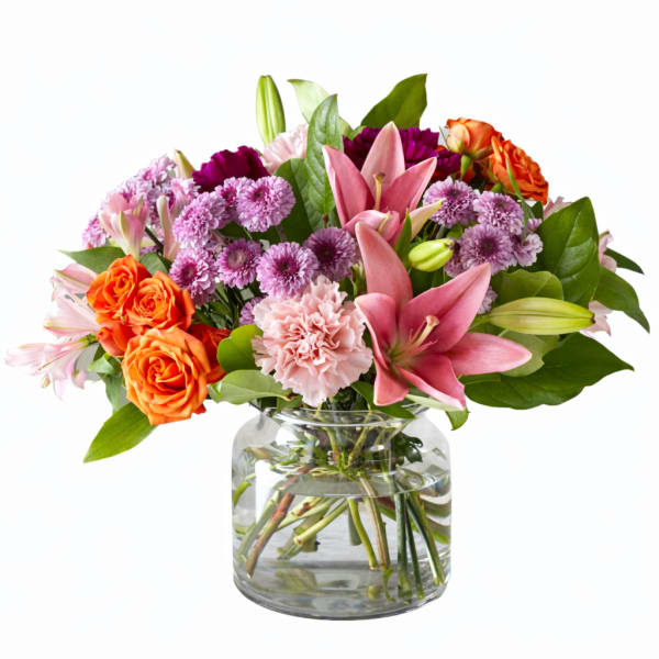 Mixed bouquet of pink lilies, orange roses, and purple flowers in a glass vase