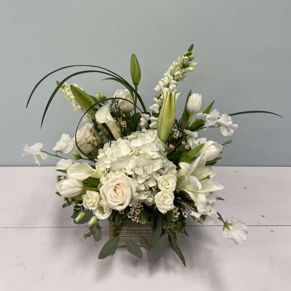 White floral arrangement with lilies, roses, and hydrangea in a square vase