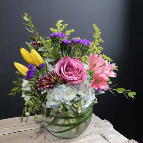 Mixed bouquet in a glass vase with a pink rose, yellow tulips, and pink alstroemeria
