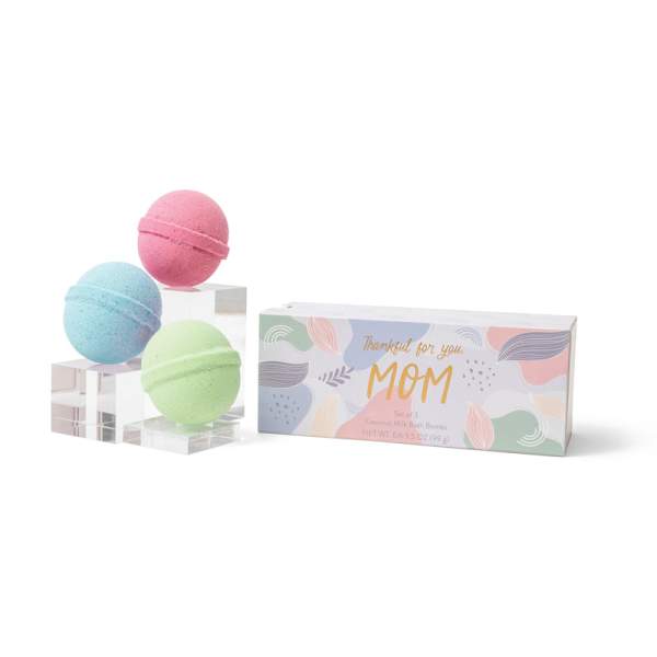 Three pastel bath bombs beside a gift box labeled for Mom