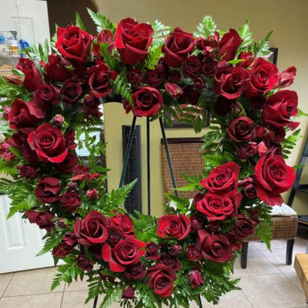 Heart-shaped wreath of red roses with abundant ferns on a standing easel