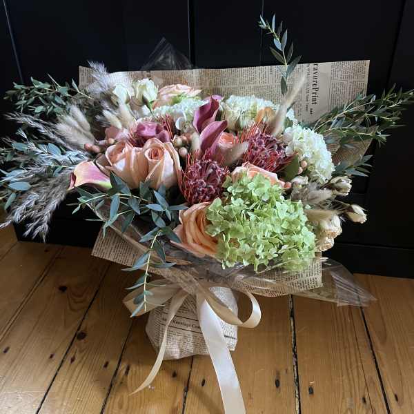 Bouquet of peach roses, hydrangeas, and dried grasses wrapped in newspaper
