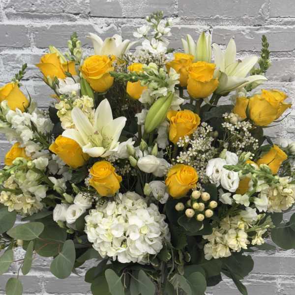Yellow roses and white lilies arranged in a clear glass vase