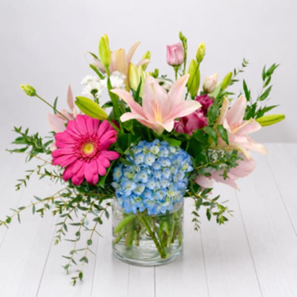 Mixed bouquet with pink lilies, blue hydrangea, and a pink gerbera daisy in a glass vase