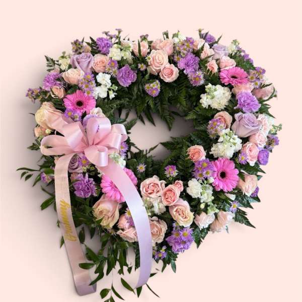 Heart-shaped floral wreath with pink, purple, and white flowers and a satin ribbon