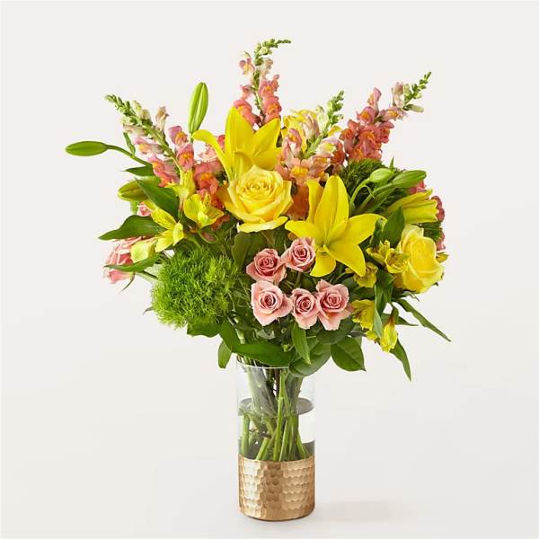 Bouquet of yellow lilies, pink roses, and snapdragons in a glass vase
