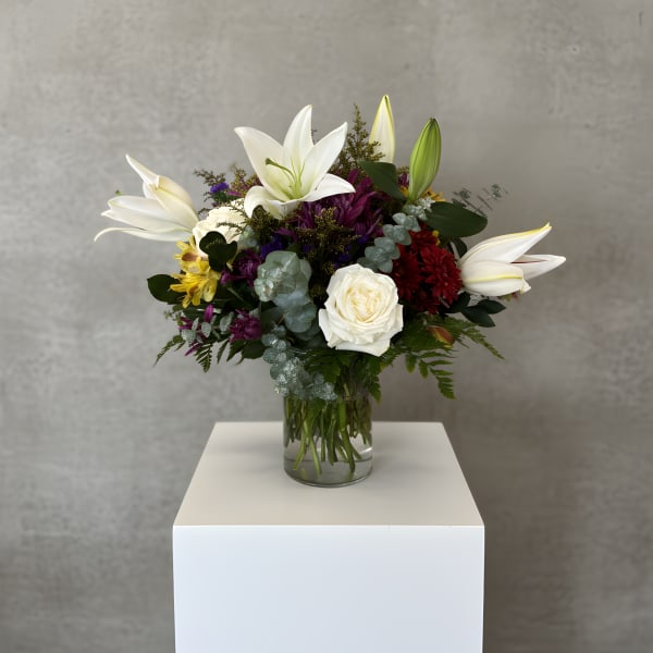 Mixed bouquet with white lilies, roses, and purple flowers in a glass vase