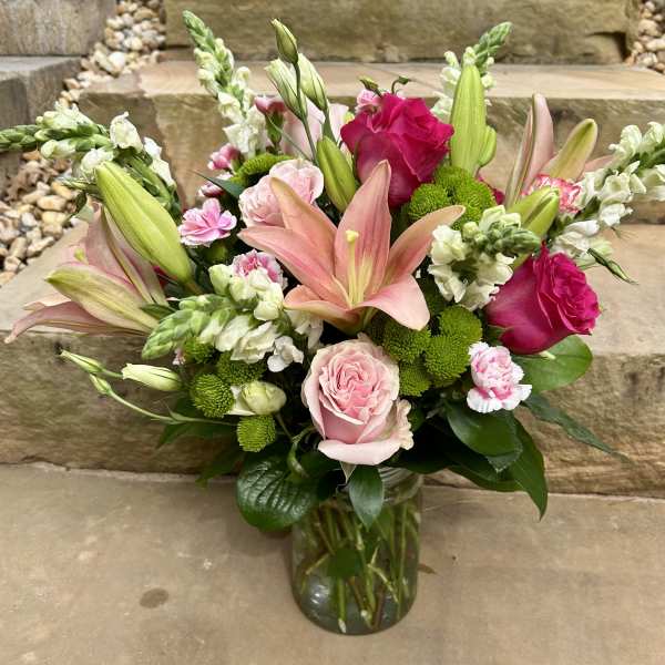Bouquet of pink lilies, roses, and green button mums in a glass vase