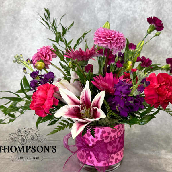 Mixed pink and purple bouquet in a clear glass vase with a ribbon