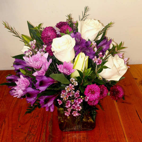 Bouquet of white roses, purple flowers, and pink blooms in a glass vase