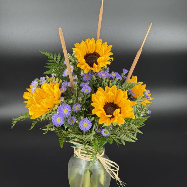Sunflowers and purple daisies in a glass vase with raffia tie