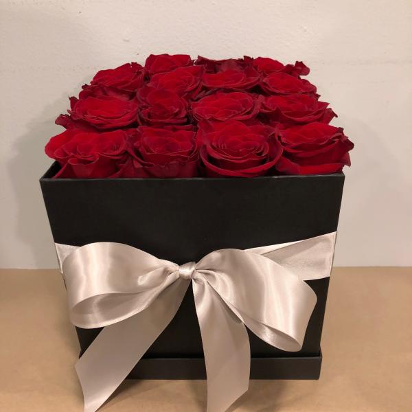 Red roses arranged in a black box with a white satin bow