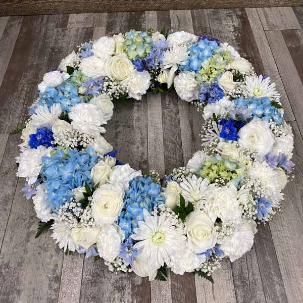 Circular floral wreath of white and blue flowers on a wood floor