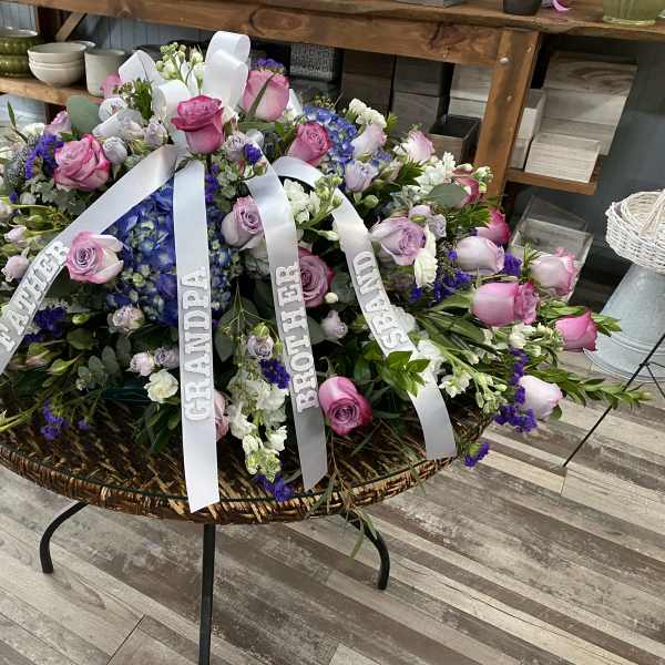 Large sympathy floral arrangement with pink and purple roses and white ribbons